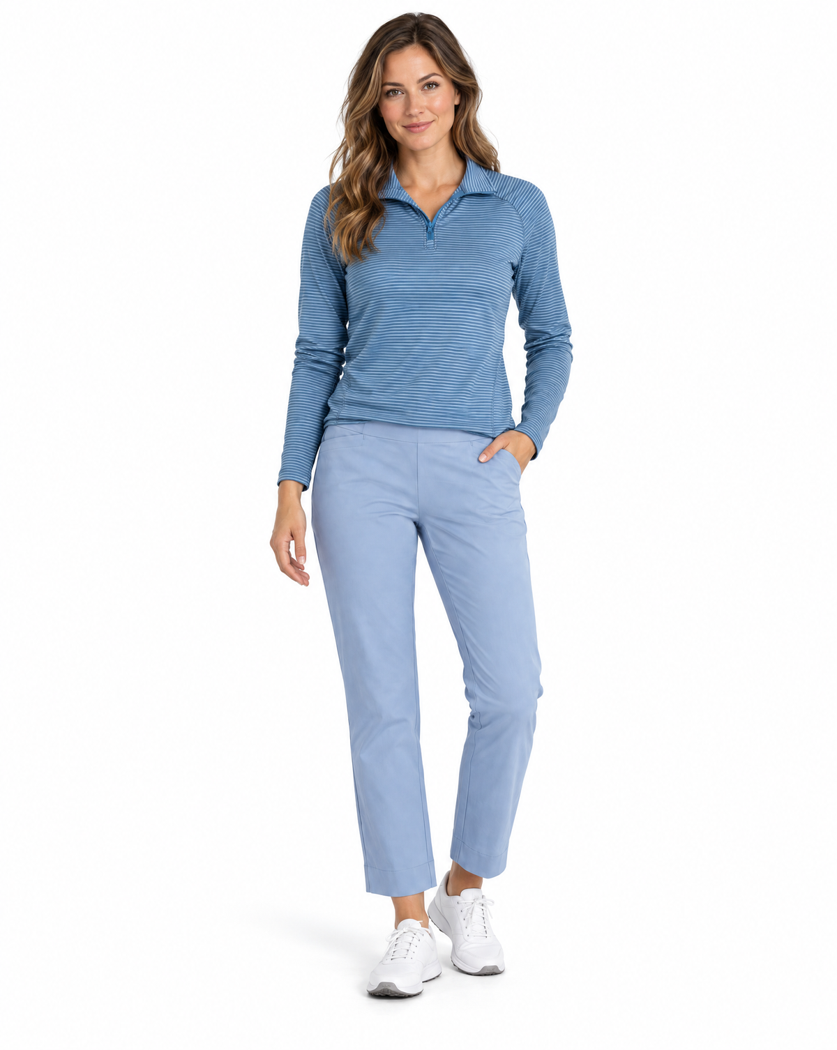A woman modeling a light blue long-sleeve quarter-zip performance top and matching light blue cropped pants, paired with white athletic sneakers, against a solid white background.