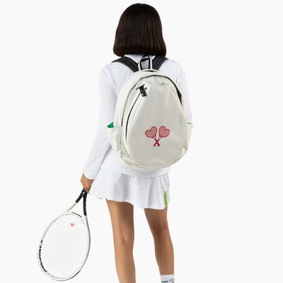 Person wearing a white outfit with a backpack holding a tennis racket on a white background