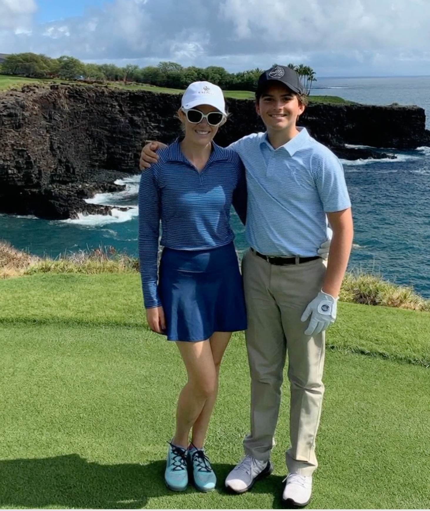 Two people posing on a golf course with ocean and cliffs in the background